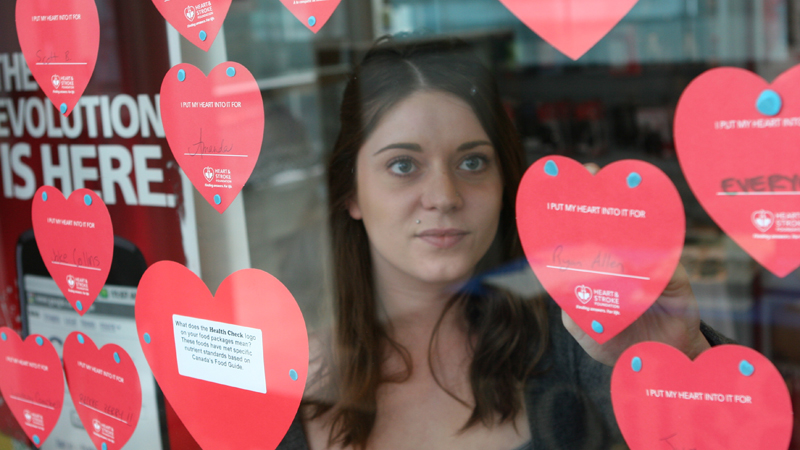 Ashley Hughes hangs a new paper heart on the Campus Store window.