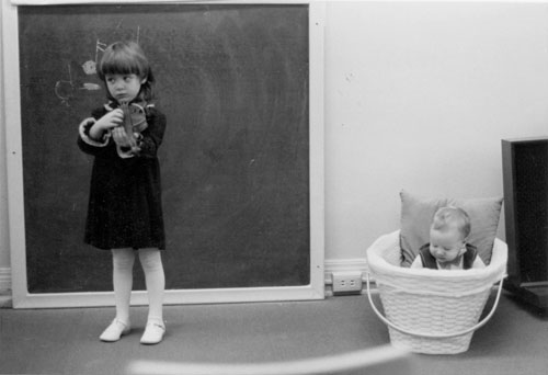A girl plays the violin with a young spectator nearby. Photo from the Bradley Institute collection.