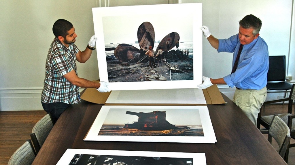 Rodman Hall Art Centre Director Stuart Reid, right, and assistant Danny Custodio handle the Burtynsky print “Shipbreaking #16, Chittagong, Bangladesh, 2000”.
