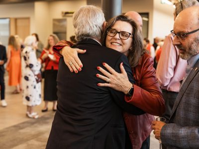A man and a woman embrace in a friendly greeting at a lively social event.