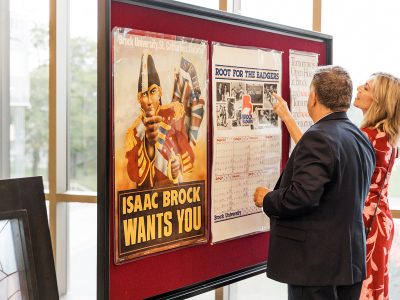 A man and a woman point at a poster on a wall display at Brock University's 60th Anniversary Skyline Celebration.