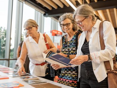 Two women look on as a third woman holds a booklet about Brock University at the Pop-up Archives display during Brock University's Skyline Celebration.