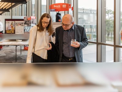 Guests at Brock University's Skyline Celebration hold cocktail glasses while looking down at a display.