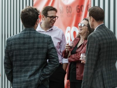 Guests at a party laugh in conversation while holding glasses of wine.