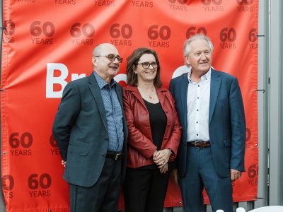 Three people pose for a photo in front of a Brock University 60th Anniversary banner.