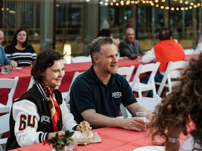 People sit at a table eating food and drinking wine while smiling in conversation.