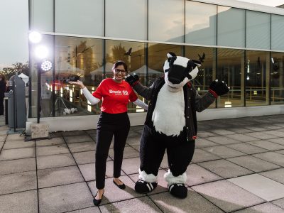 A woman smiles and holds her arms up while standing next to Brock University's mascot Boomer the Badger.