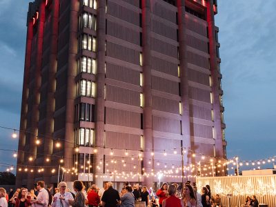 Guests mingle under the night sky and strings of twinkle lights at Brock University's Skyline Celebration, Arthur Schmon Tower stands in the background.