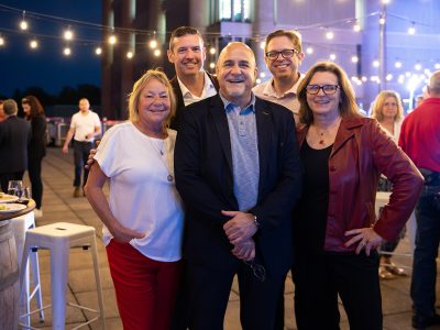 Five people pose for a group photo at an evening outdoor party.