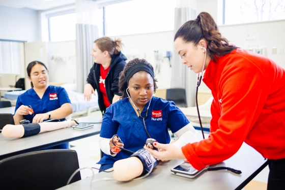 Nursing students and teacher working on a simulated blood pressure arm