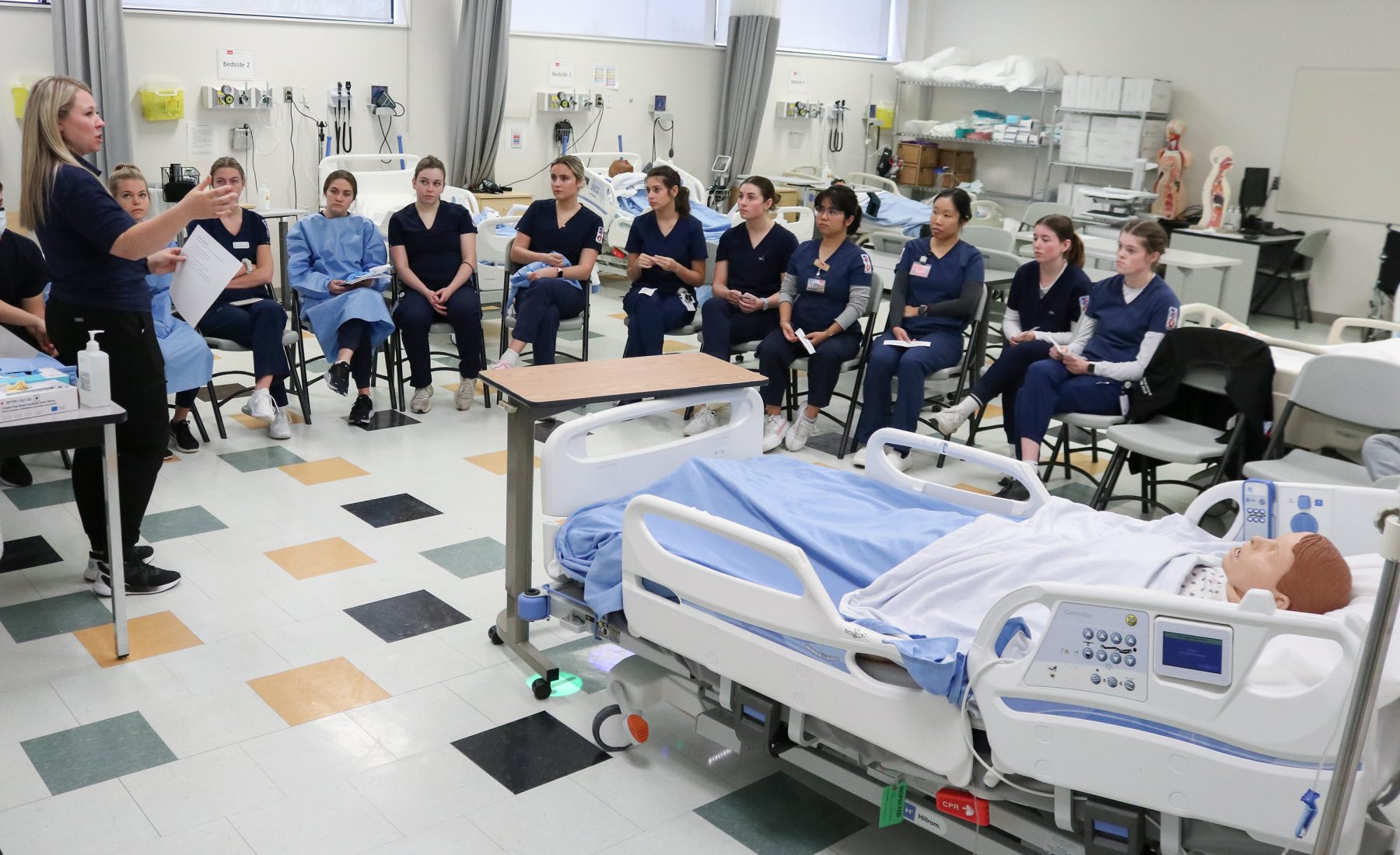 Nursing students sit in a semi circle around a patient simulator 