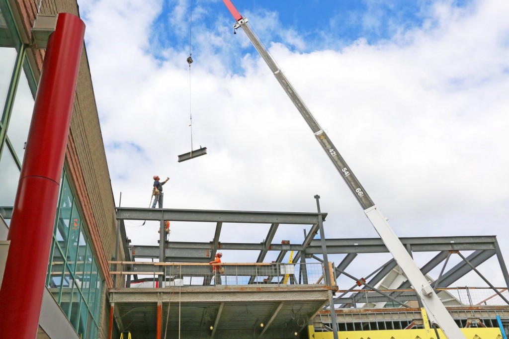Construction workers work to install the final beam into the framework of the Goodman School of Business building. 