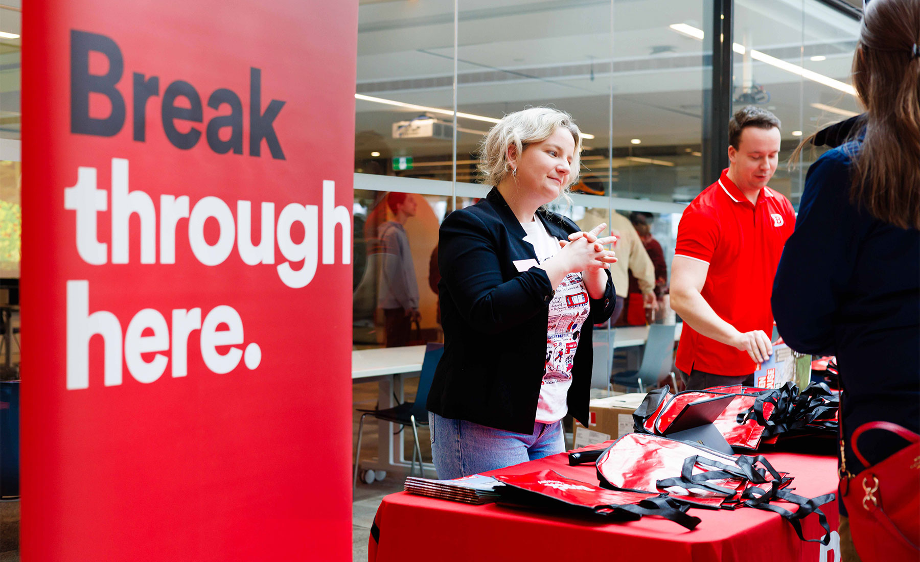 visual-elements1 People chat with attendees at a booth at Brock University Spring Open House with a red banner reading "Break through here."