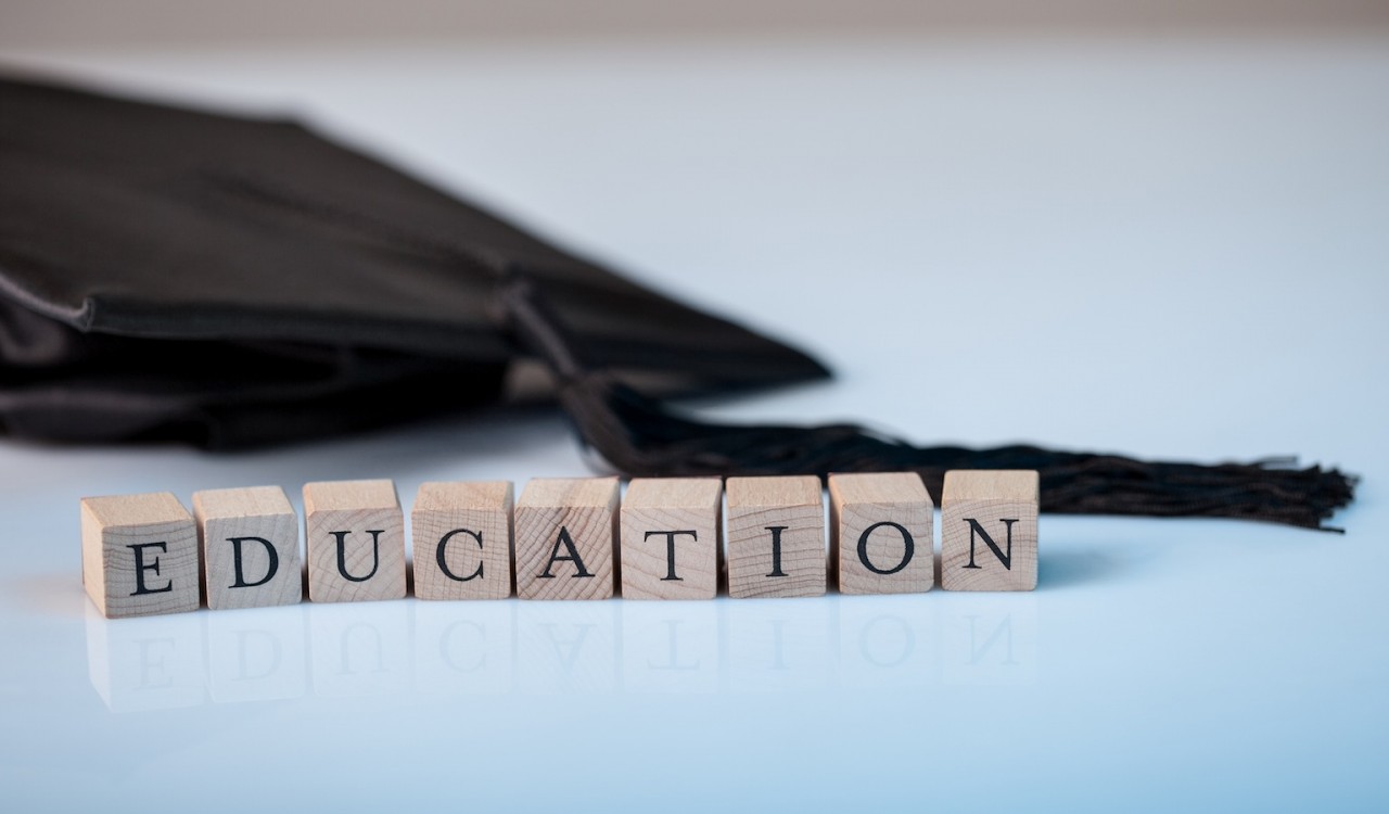 Education concept with the alphabet letters for Education spelt out on wooden blocks beside a graduation cap