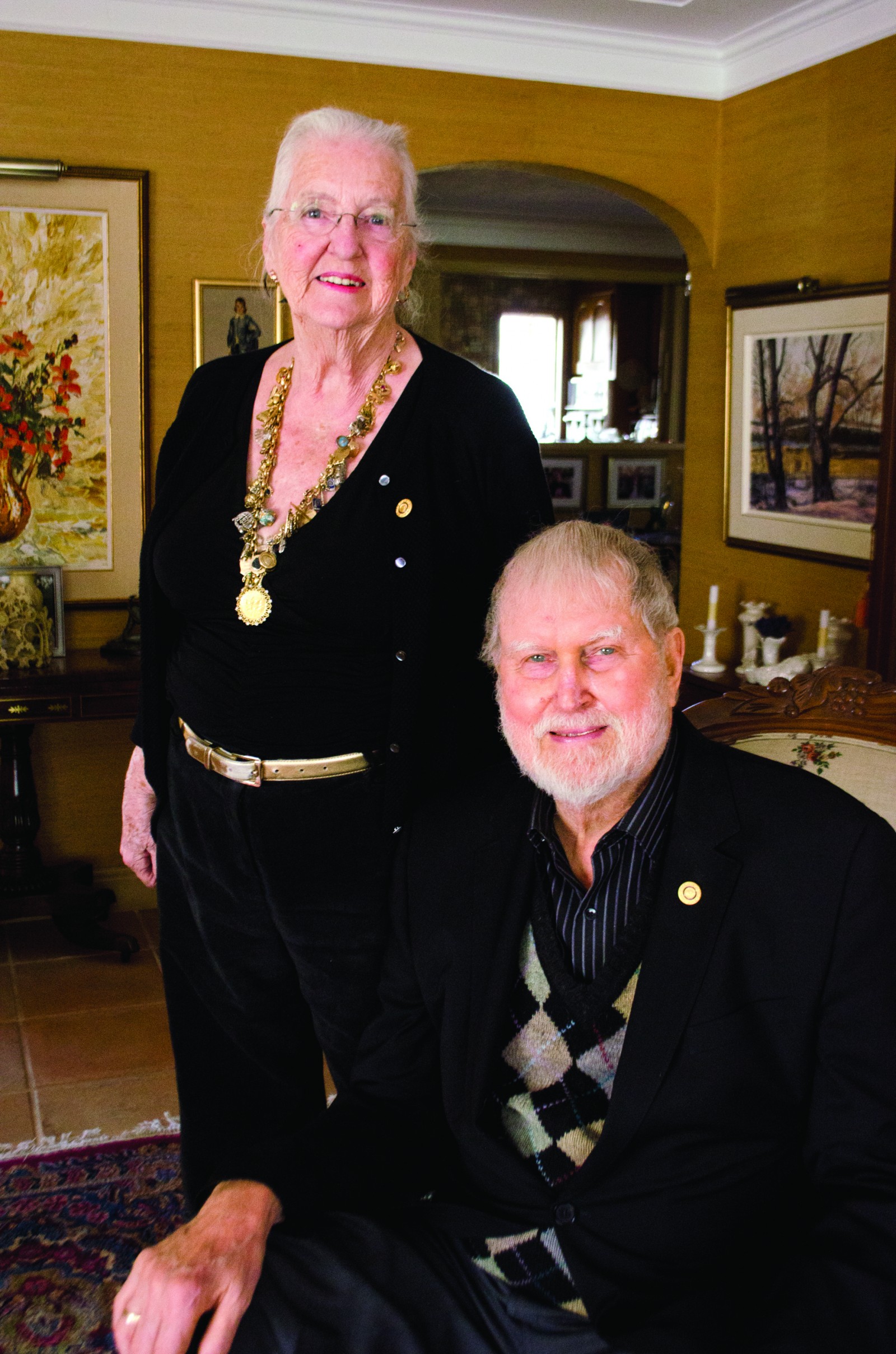 Val and Art Fleming in their home in Beamsville. Val stands next to Art, who is sitting. (photo supplied by Grimsby Lincoln News/Niagara this Week)
