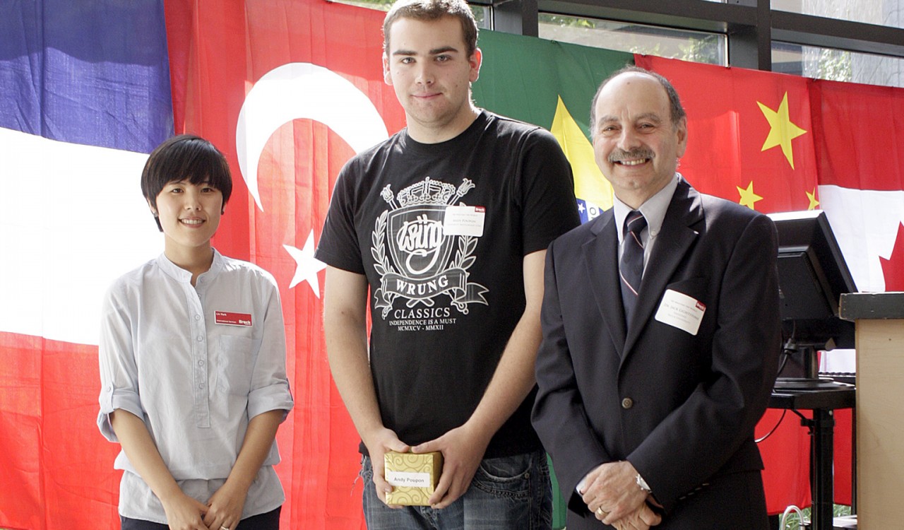 UM participant Andy Poupon, middle, receiving a gift from President Jack Lightstone and Liv Park, Scholar Services and Program Assistant at the We Welcome the World reception this summer.