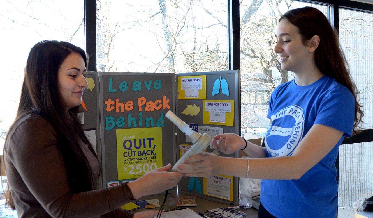 Isabella Churchill, Campus Coordinator for Leave the Pack Behind is teaching student volunteer Andrea Sacco how to show students the correct way to use and read the results of the LTPB carbon monoxide detector, a teaching tool which measures the carbon monoxide levels in a person’s lungs.