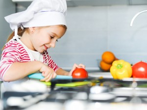 A young girl in a chef's hat chops vegetables