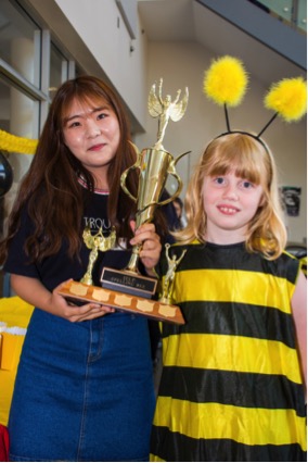 Eunju Lee gets her Spelling Bee trophy from mascot Sophie Sekel, a contest judge, Wednesday.