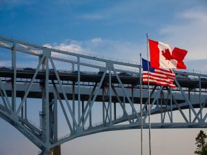 A metal bridge crossing with the U.S. and Canada flags flying from flagpoles in the foreground.