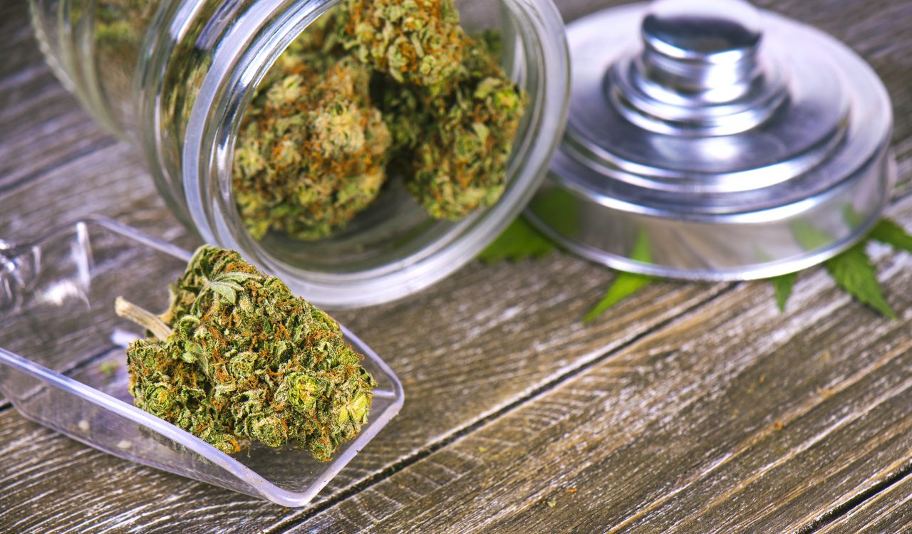 Cannabis buds sitting on a wooden table in a glass jar.