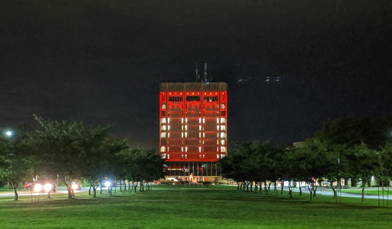 A large square building illuminated with red lights..