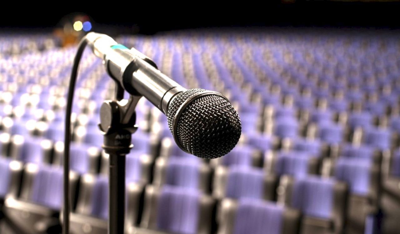 A microphone in the foreground with empty auditorium seats in the background.