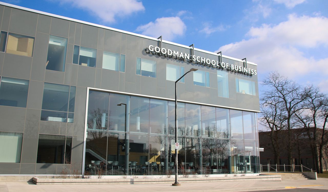 A grey and glass building is pictured with the words Goodman School of Business across the top.