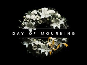 A wreath with white flowers and a yellow ribbon has the words “Day of Mourning” written across it.