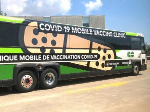 A green bus that functions as a mobile vaccination clinic sits in a parking lot.