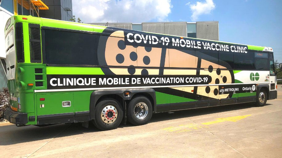 There is a green bus in the parking lot that acts as a mobile vaccination clinic.