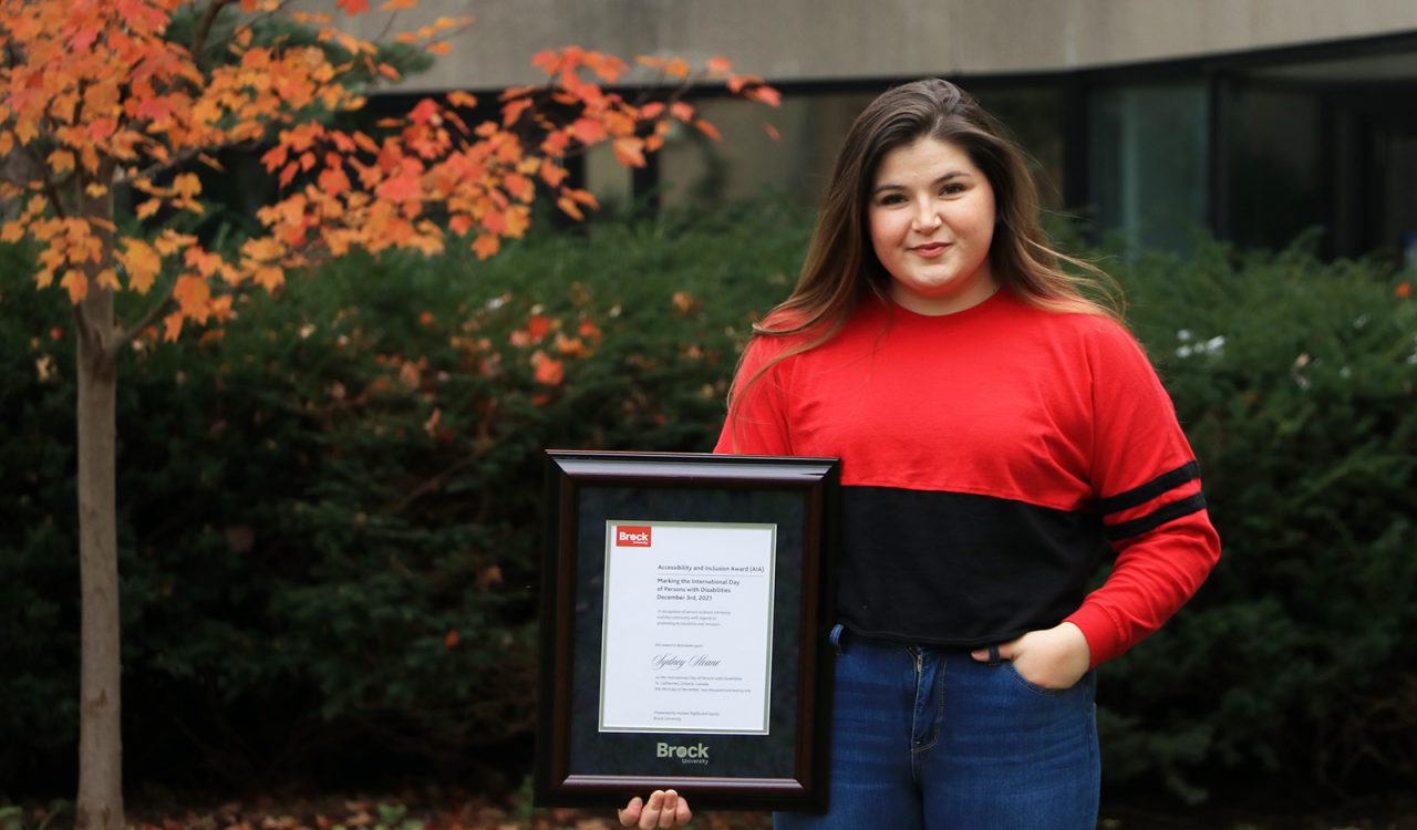 Fourth-year Physical Education student Sydney Sloane is shown holding a framed certificate of Brock University's Accessibility and Inclusion Recognition Award.