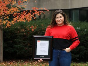 Fourth-year Physical Education student Sydney Sloane is shown holding a framed certificate of Brock University's Accessibility and Inclusion Recognition Award.