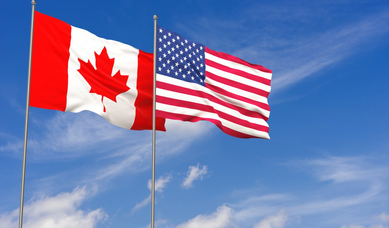 The Canadian and U.S. flags flying against a bright blue sky.