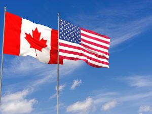 The Canadian and U.S. flags flying against a bright blue sky.