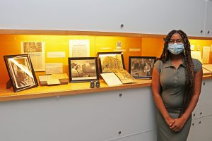 A woman stands in front of a long, lighted display case that contains books, photographs and newspaper clippings.