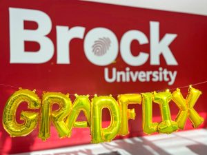 Letter shaped balloons spelling out 'GRADflix' in front of the Brock University logo