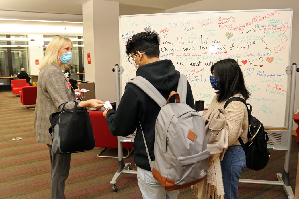 Brock University Interim President Lynn Wells hands coffee vouchers to two students in the Brock Library