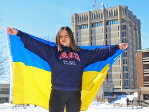 A student holding a Ukrainian flag in front of Schmon Tower.