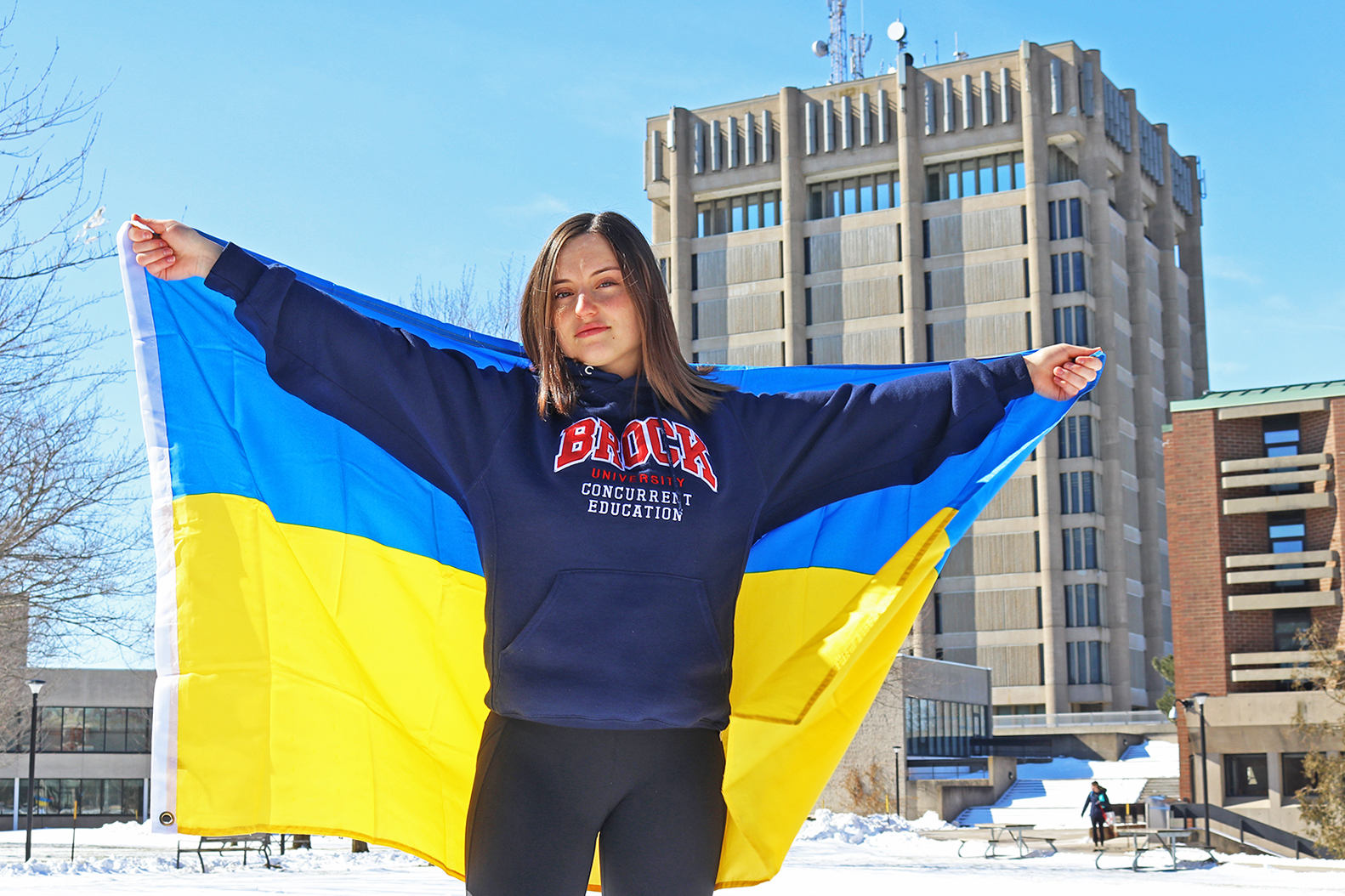 A student holding a Ukrainian flag in front of Schmon Tower.