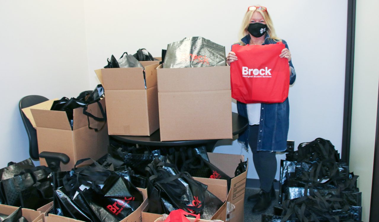 A woman holds a red bag in a room full of packed boxes and bags