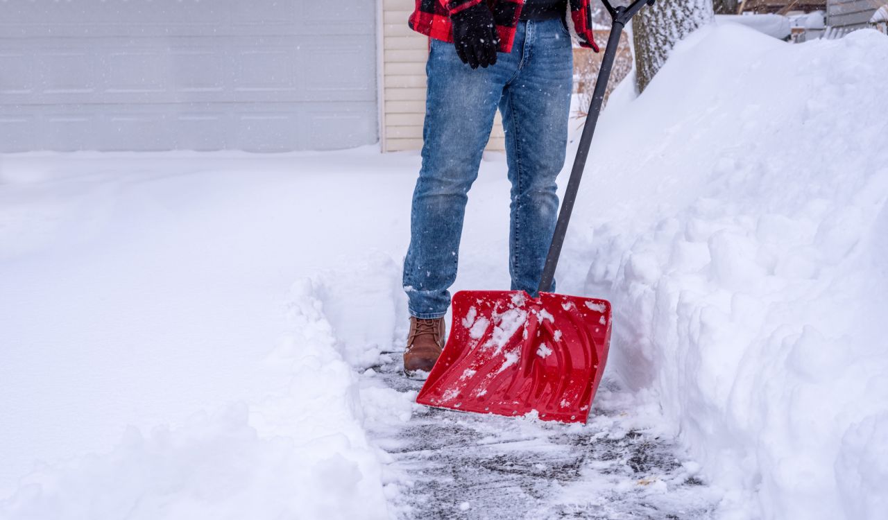 A man shovelling deep snow by hand with a red snow shovel