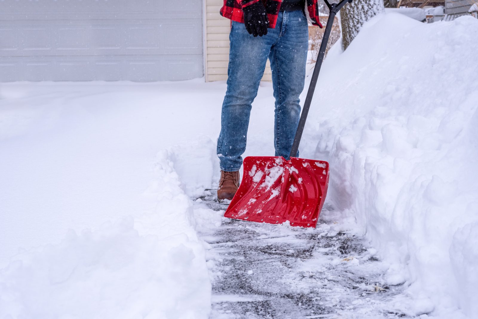 A man shovelling deep snow by hand with a red snow shovel