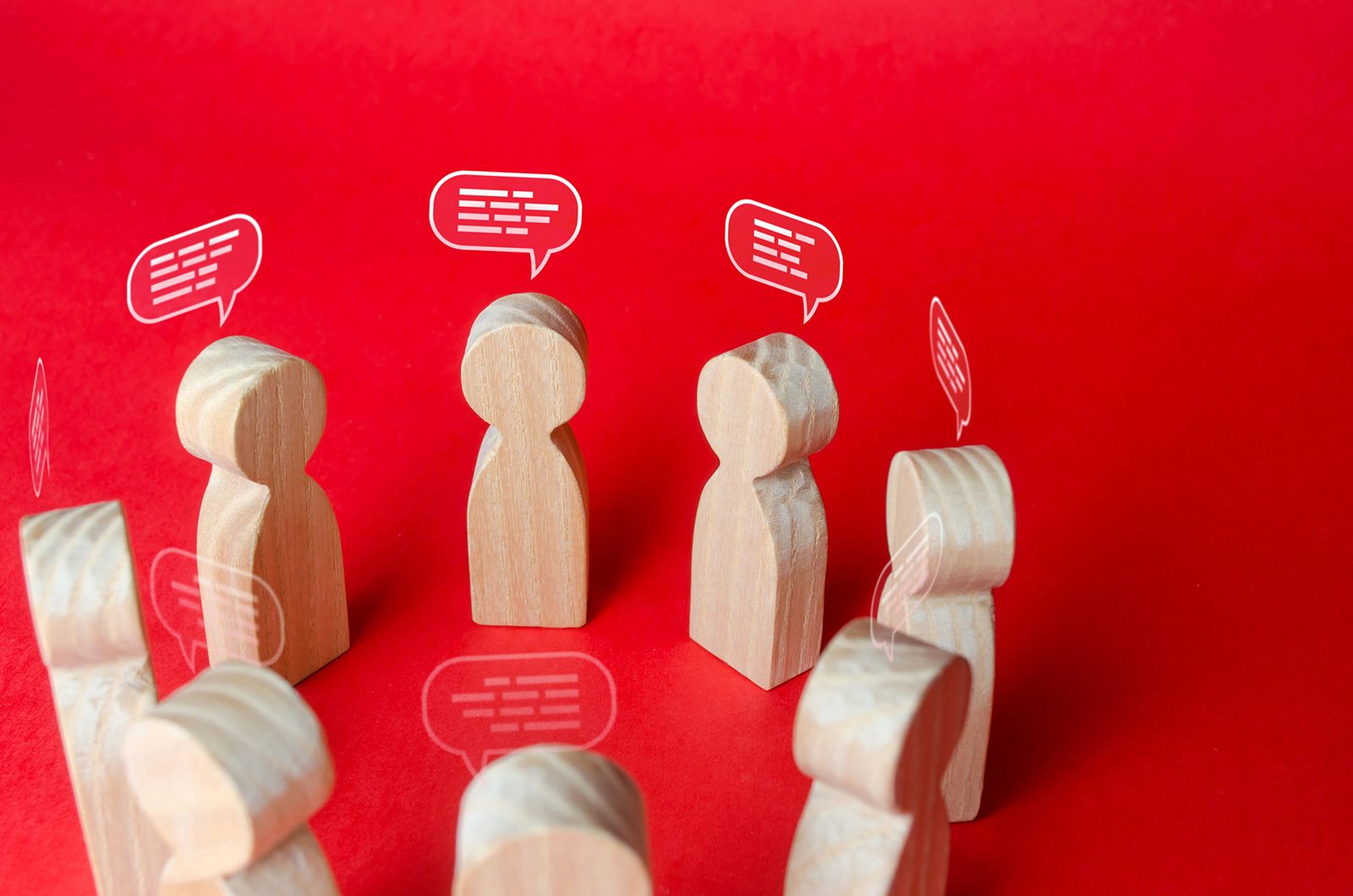 Eight wooded peg people form a circle. Illustrated white speech bubbles are over their heads, suggesting they are having a group discussion.