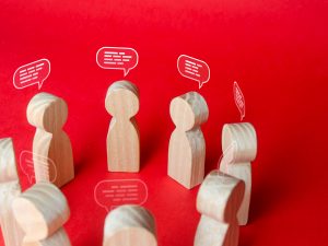 Eight wooded peg people form a circle. Illustrated white speech bubbles are over their heads, suggesting they are having a group discussion.