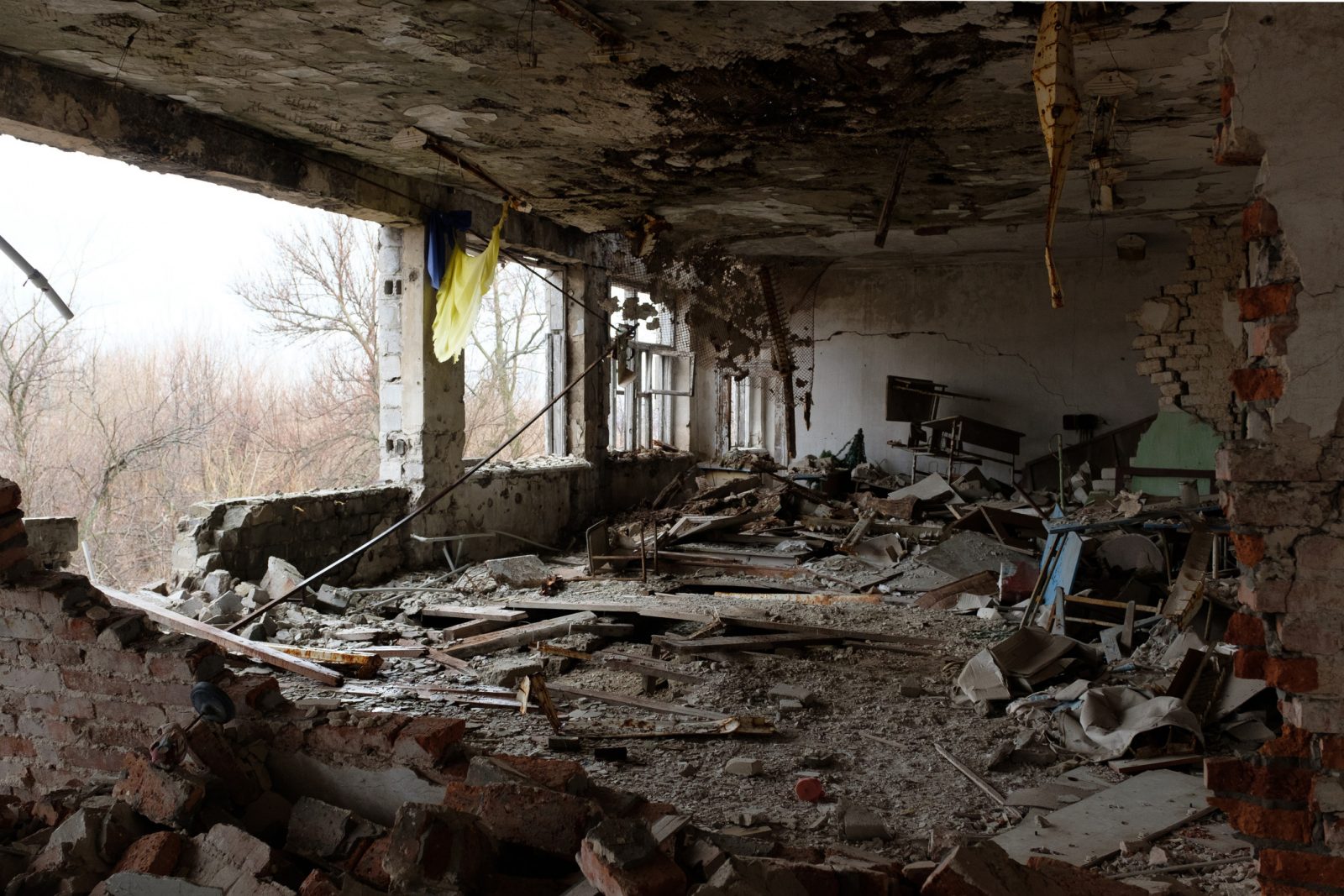 The inside view of the remains of a building that was bombed, with blackened debris hanging from the ceiling and chunks of wood and concrete scattered across the floor.