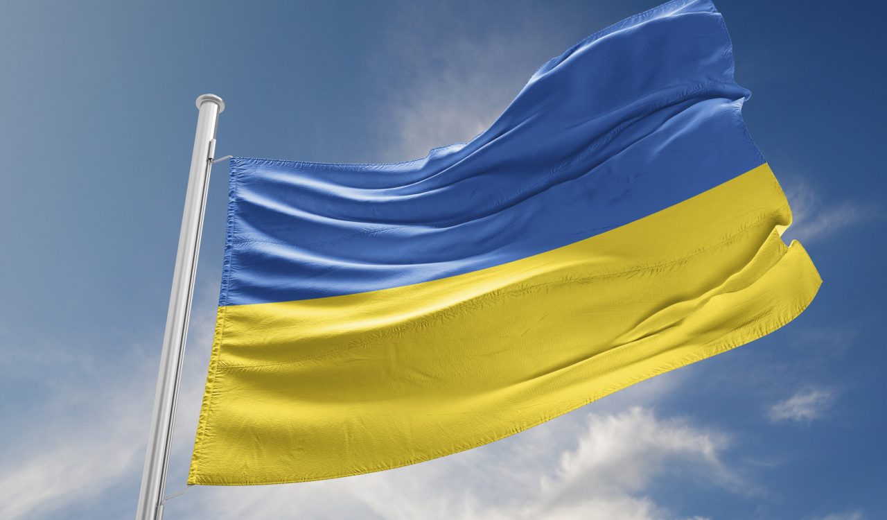 The blue and yellow flag of Ukraine flies against a bright blue sky.