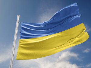The blue and yellow flag of Ukraine flies against a bright blue sky.