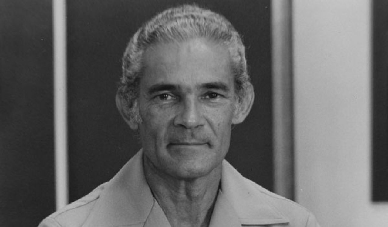 Monochrome portrait of Michael Manley with arms folded.