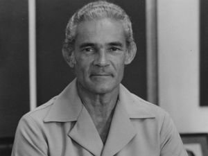 Monochrome portrait of Michael Manley with arms folded.